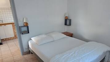 A bedroom with a bed, a nightstand, a wall-mounted lamp, and a bathroom visible through an open door.