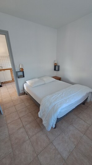 A bedroom with a bed, a nightstand, a wall-mounted lamp, and a bathroom visible through an open door.