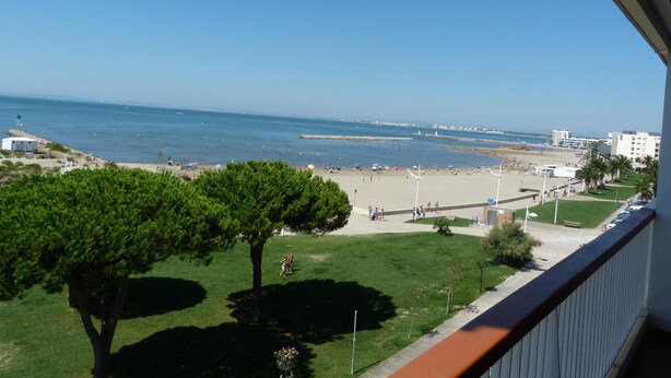 Een balkon met uitzicht op een strand, een gazon en een helderblauwe lucht.