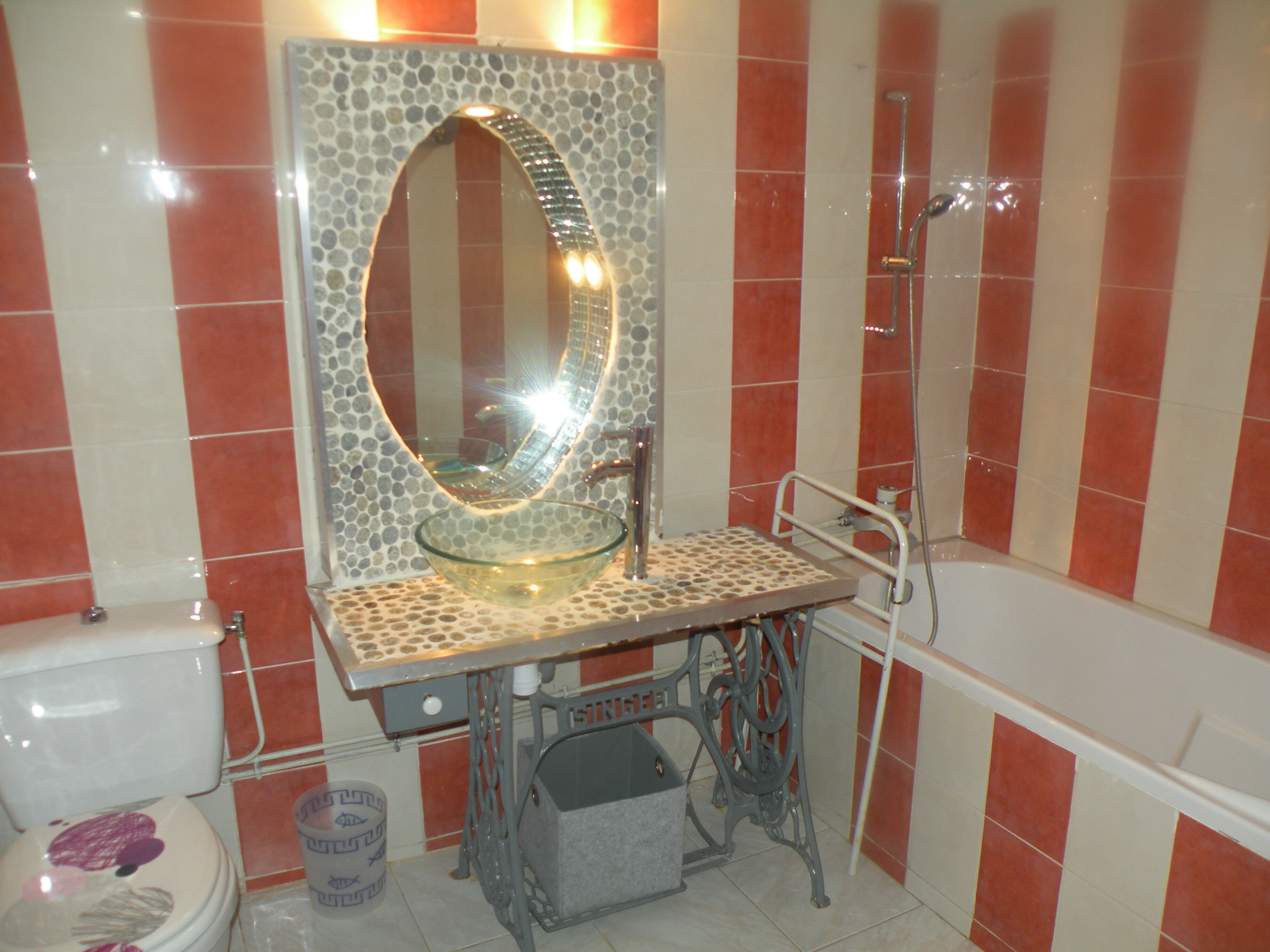 A bathroom with a toilet, a sink with a mosaic mirror, and a bathtub.