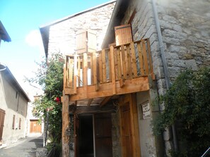 A wooden balcony attached to a stone building with a sign indicating a business name and contact number.