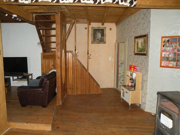 A wooden interior with a staircase, a television, a leather chair, and a small wooden shelf with various items.