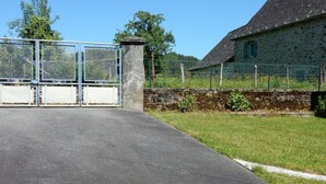 A gated entrance with a metal fence, a stone pillar, and a building with a stone wall and a window. - Colorful house in a green hamlet (Forgès)