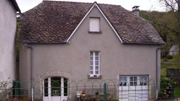 A two-story house with a stone roof, a front door, and a small garden with pink flowers. - Colorful house in a green hamlet (Forgès)