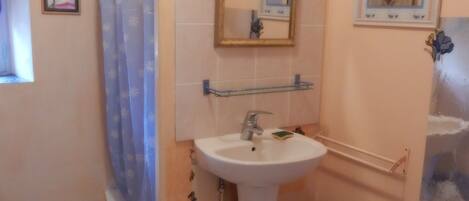 A bathroom with a pedestal sink, a shower curtain, a mirror, and a small trash bin.
