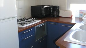 Une cuisine de taille réduite avec des meubles bleus, une cuisinière à gaz, un four à micro-ondes, un grille-pain et un évier.