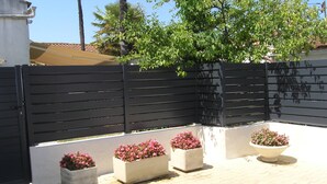 Une cour avec une clôture noire, des plantes en pot ornées de fleurs roses et un arbre.