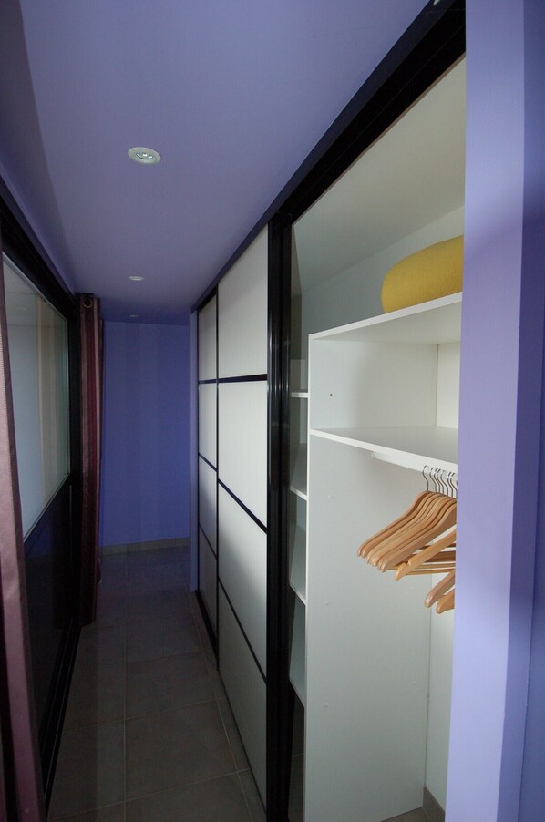 A narrow hallway with a sliding closet door, a tiled floor, and a window with curtains.