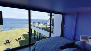Un dormitorio con un ventanal grande que da a un balcón y al mar.