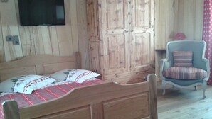 Ein hölzernes Bett mit Karo-Bettdecke, ein Holzschrank, ein an der Wand befestigter Fernseher und ein Sessel mit Kissen.