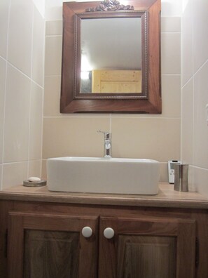 Un baño con tocador de madera, un lavabo blanco y un espejo encima.
