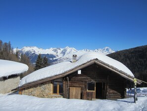 Een houten hut met een stenen fundering, omgeven door met sneeuw bedekte bergen en bomen.