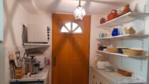 A compact kitchen with white cabinets, a wooden door, and shelves holding kitchenware and decorative items. - Sea views, 2 beautiful terraces, charming duplex in villa, landscaped garden   (Brando)