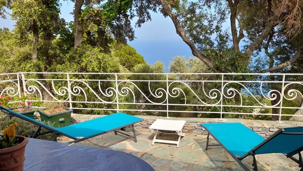 A terrace with two blue lounge chairs and a small table, surrounded by a white decorative fence and stone flooring, overlooking a scenic view. - Sea views, 2 beautiful terraces, charming duplex in villa, landscaped garden   (Brando)