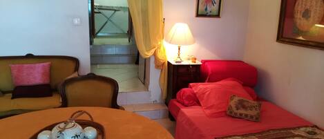 Une pièce avec un canapé, un lit rouge, une lampe, un tableau et un plateau avec des théières.