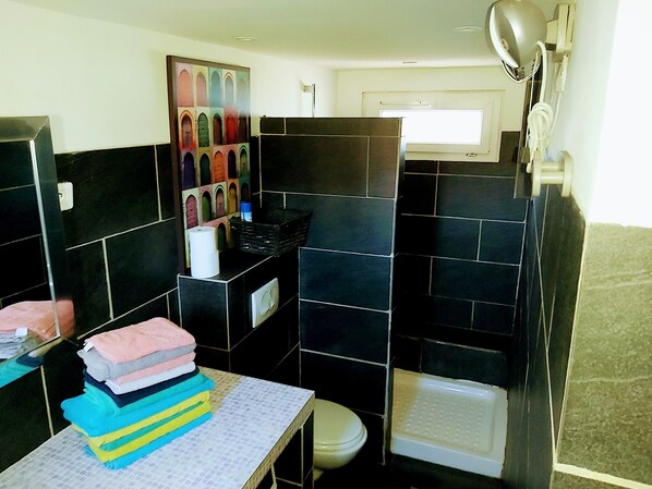A bathroom with black tiles, a sink, a toilet, and a shower area.