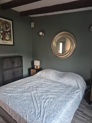 Une chambre à coucher avec un grand lit, une commode, un miroir rond et une œuvre d’art encadrée accrochée au mur.