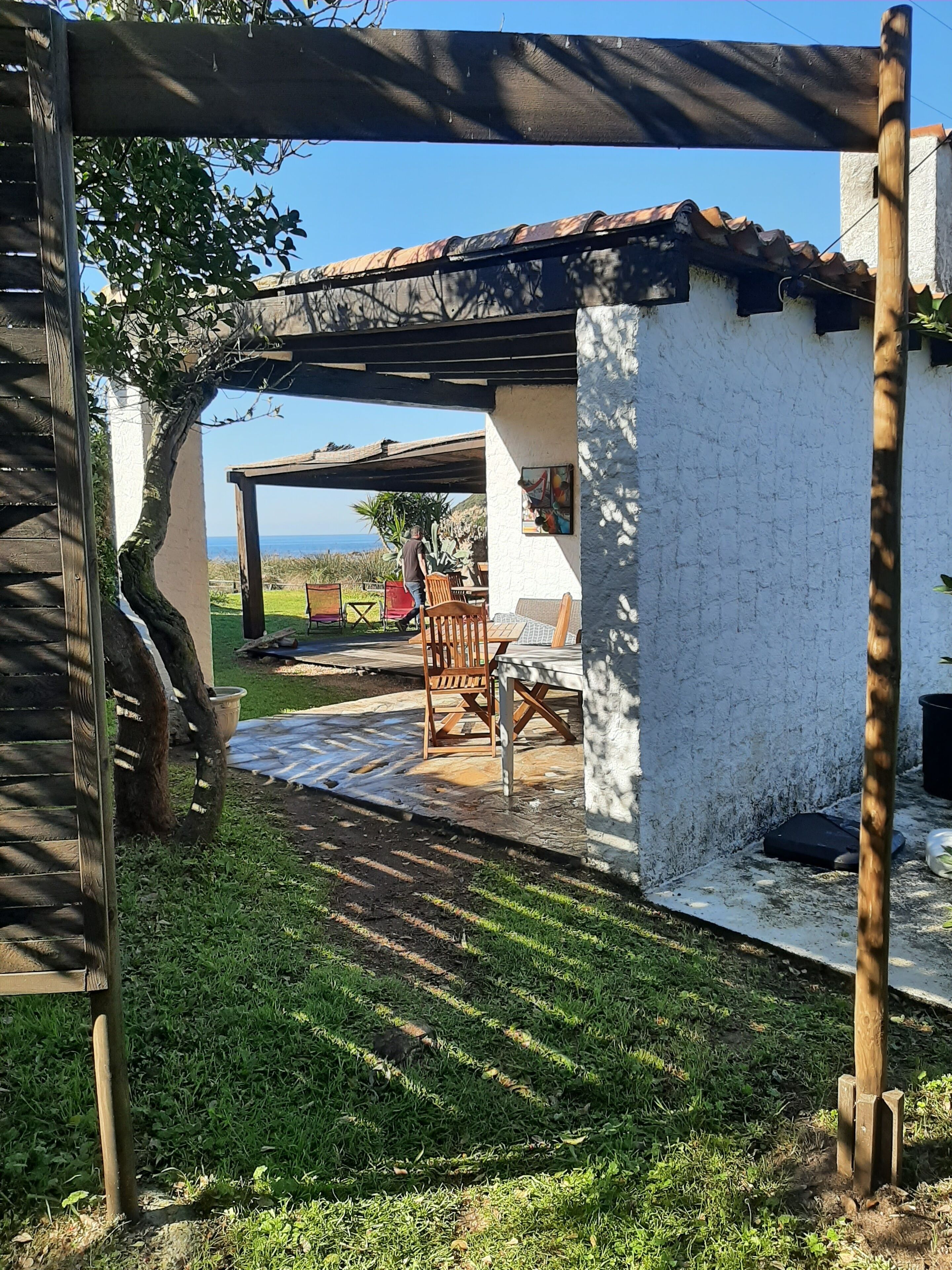 Un patio couvert avec une table et des chaises, un mur blanc et une vue sur la mer.