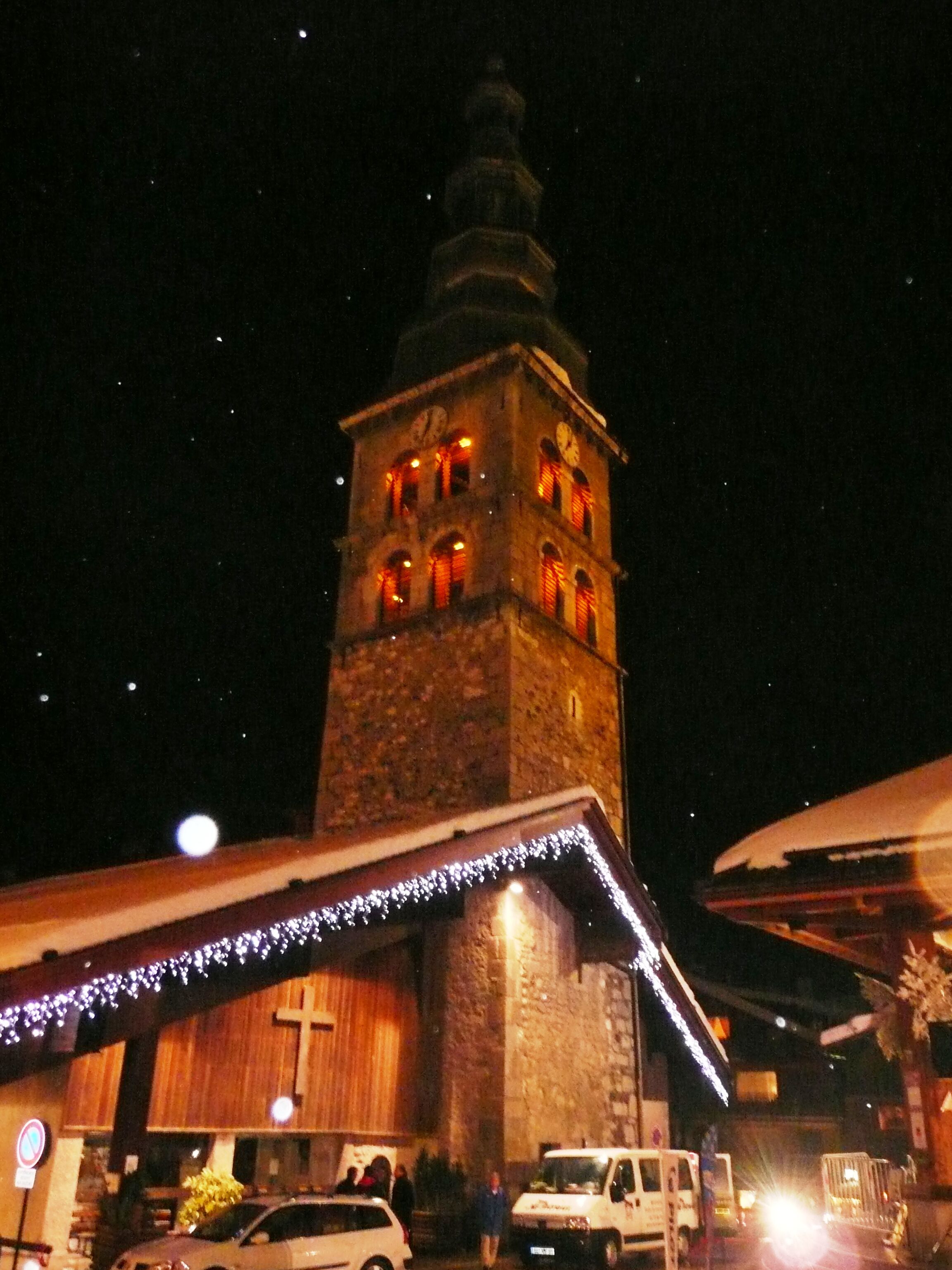 A historic building with a clock tower, a cross, and a bell.