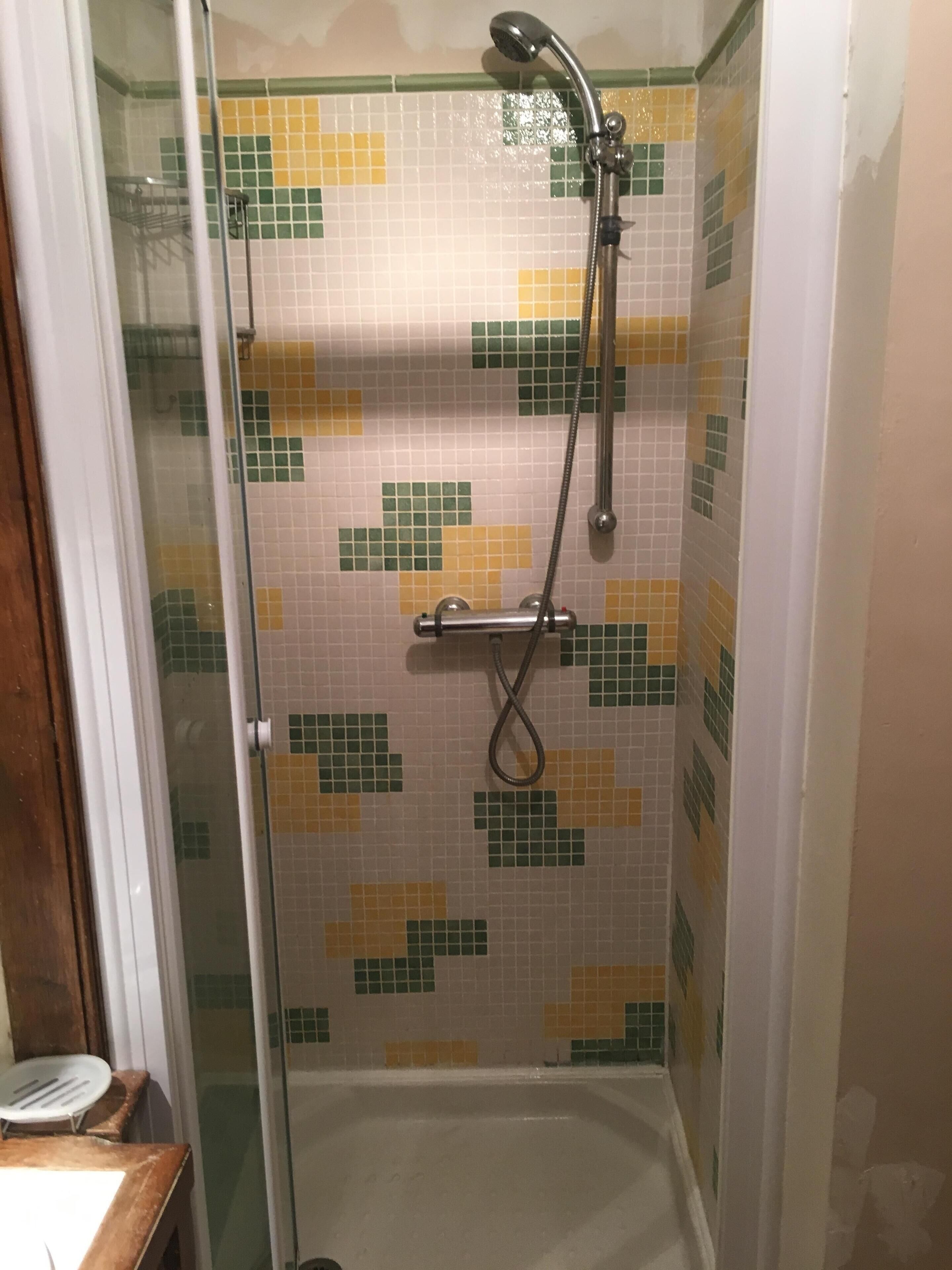 Una ducha con puerta de vidrio, paredes de azulejos y cabezal de ducha de mano.