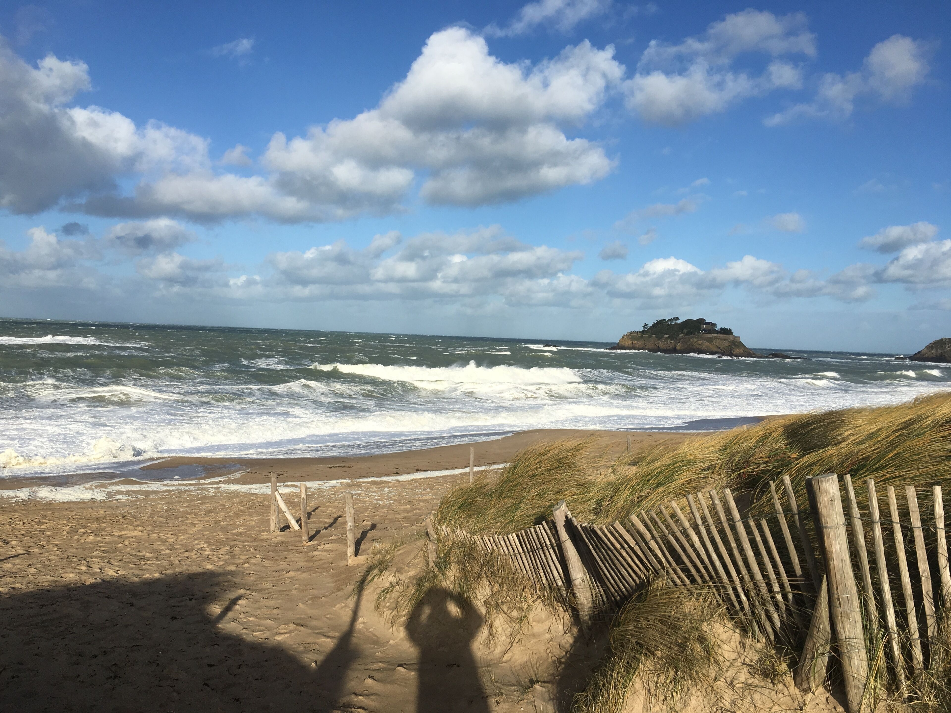 A beach with waves, a wooden fence, and a rocky outcrop in the distance.