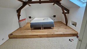 A bedroom with a sloped ceiling, wooden beams, a bed, and a skylight.