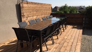Eine Holzterrasse mit einem Glastisch und schwarzen Stühlen.