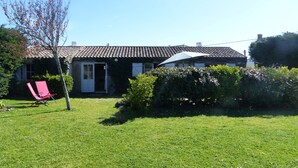 Een huis met een pannendak, een deur en een kleine tuin met een stoel en struiken.