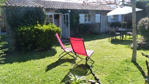 Een huis met een pannendak, een deur en een raam. Er staat een rode stoel en een tafel met stoelen buiten.