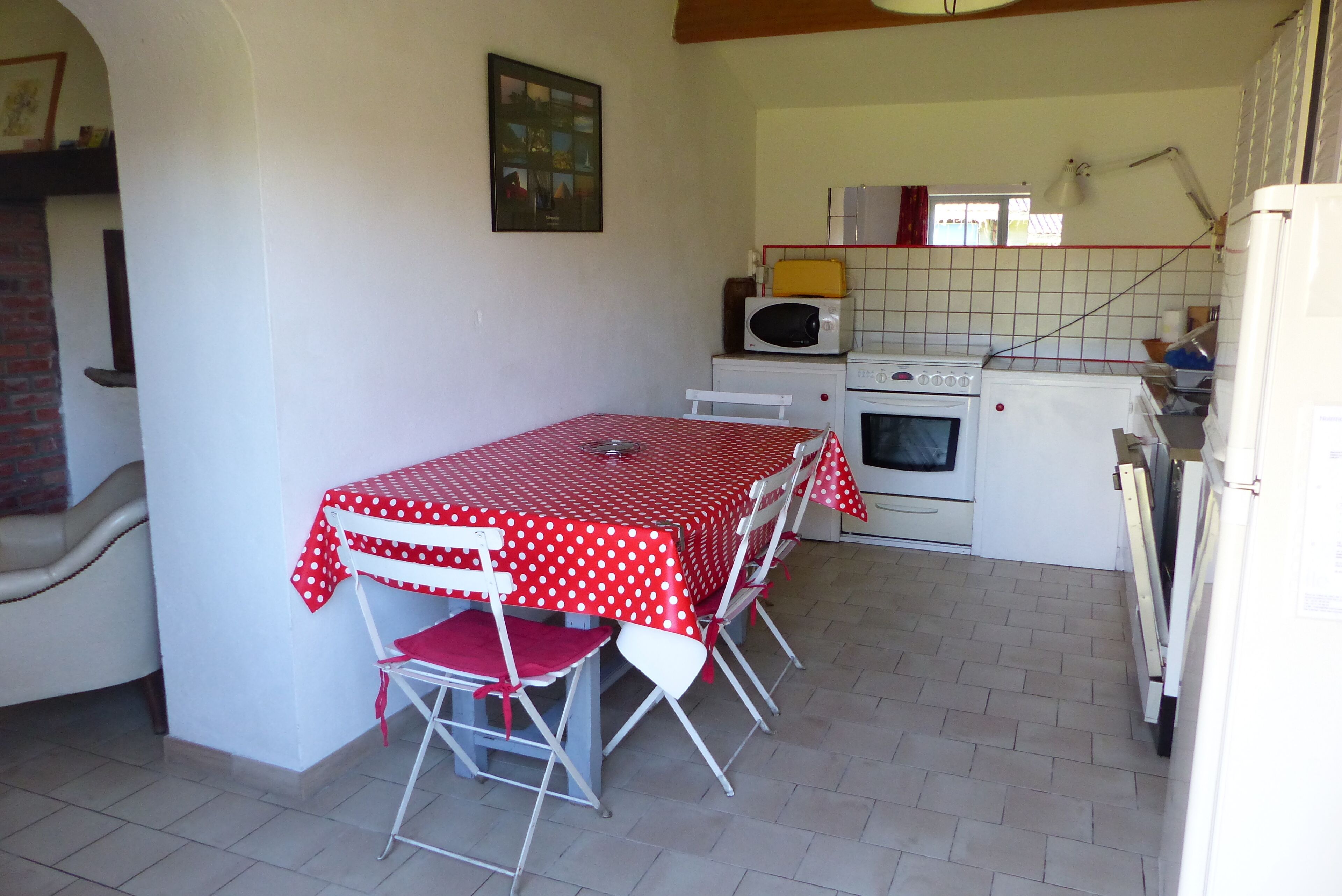 A kitchen with a dining table covered in a red and white polka dot tablecloth, a microwave, an oven, and a refrigerator.