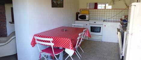 A kitchen with a dining table covered in a red and white polka dot tablecloth, a microwave, an oven, and a refrigerator.