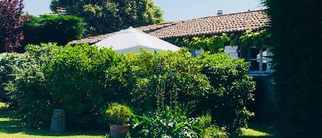 Un jardín con una sombrilla blanca, un monumento de piedra y un edificio con tejado de baldosas.