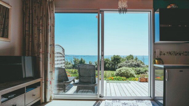A room with a sliding glass door leading to a deck with a view of the ocean. - House direct access to the beach from the garden. (Trébeurden)