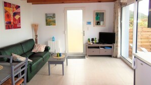 A living room with a green sofa, a coffee table, a TV on a cabinet, and a door leading outside. - House direct access to the beach from the garden. (Trébeurden)