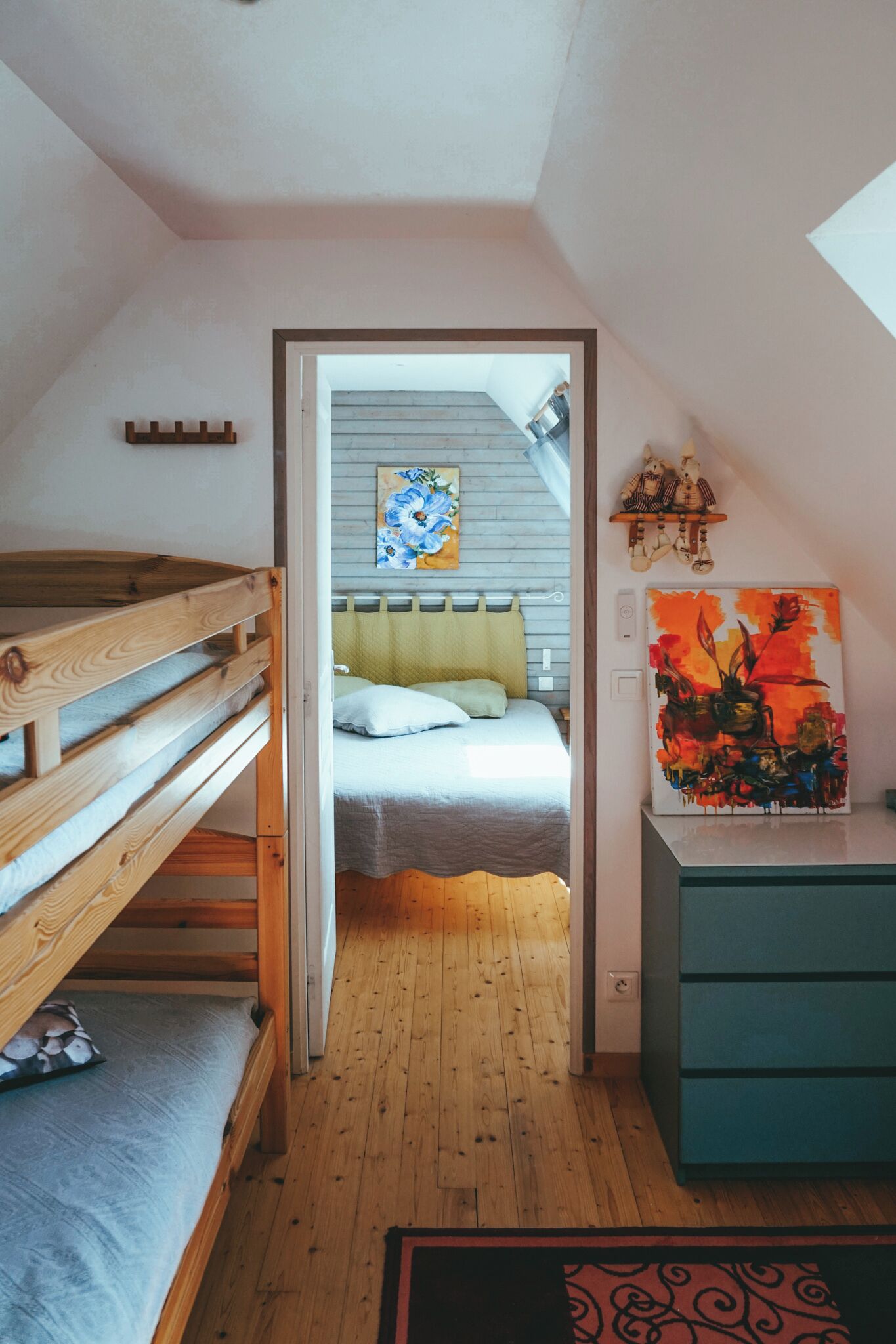 Ein Zimmer mit einem Etagenbett, einem Bett mit gelbem Kopfteil, einem Gemälde und einem Schrank.