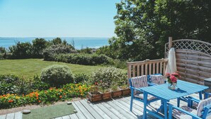 A wooden deck with a table and chairs, surrounded by a garden with various plants and flowers. - House direct access to the beach from the garden. (Trébeurden)