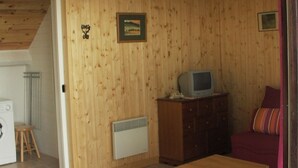 Ein Zimmer mit Holzwänden, einem kleinen Tisch, einem Fernseher auf einem Schrank und einem roten Sofa.
