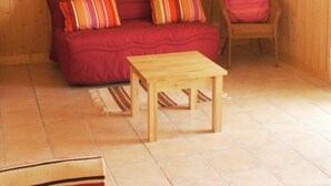 Ein gemütliches Zimmer mit einer Holzwand, einem roten Sofa mit gestreiften Kissen, einem Holztisch und einem Korbstuhl.