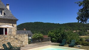 A stone house with a swimming pool, outdoor seating, and a view of a forested hill. - Renovated house in black Périgord with private pool and wifi for 6/8 people (Montignac)