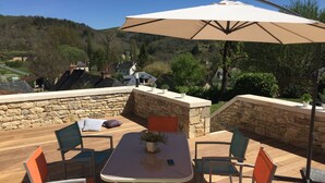 A wooden deck with a table and chairs, an umbrella, and a stone wall. - Renovated house in black Périgord with private pool and wifi for 6/8 people (Montignac)
