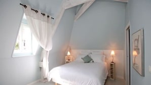 A bedroom with a sloped ceiling, a bed with white bedding, two bedside lamps, and a window with white curtains. - Renovated house in black Périgord with private pool and wifi for 6/8 people (Montignac)