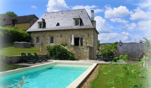 Una casa in pietra con piscina, giardino e un muro di pietra.