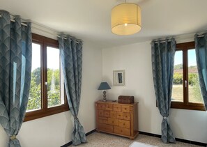 A room with two windows, a wooden dresser, a lamp, and a hanging light fixture.