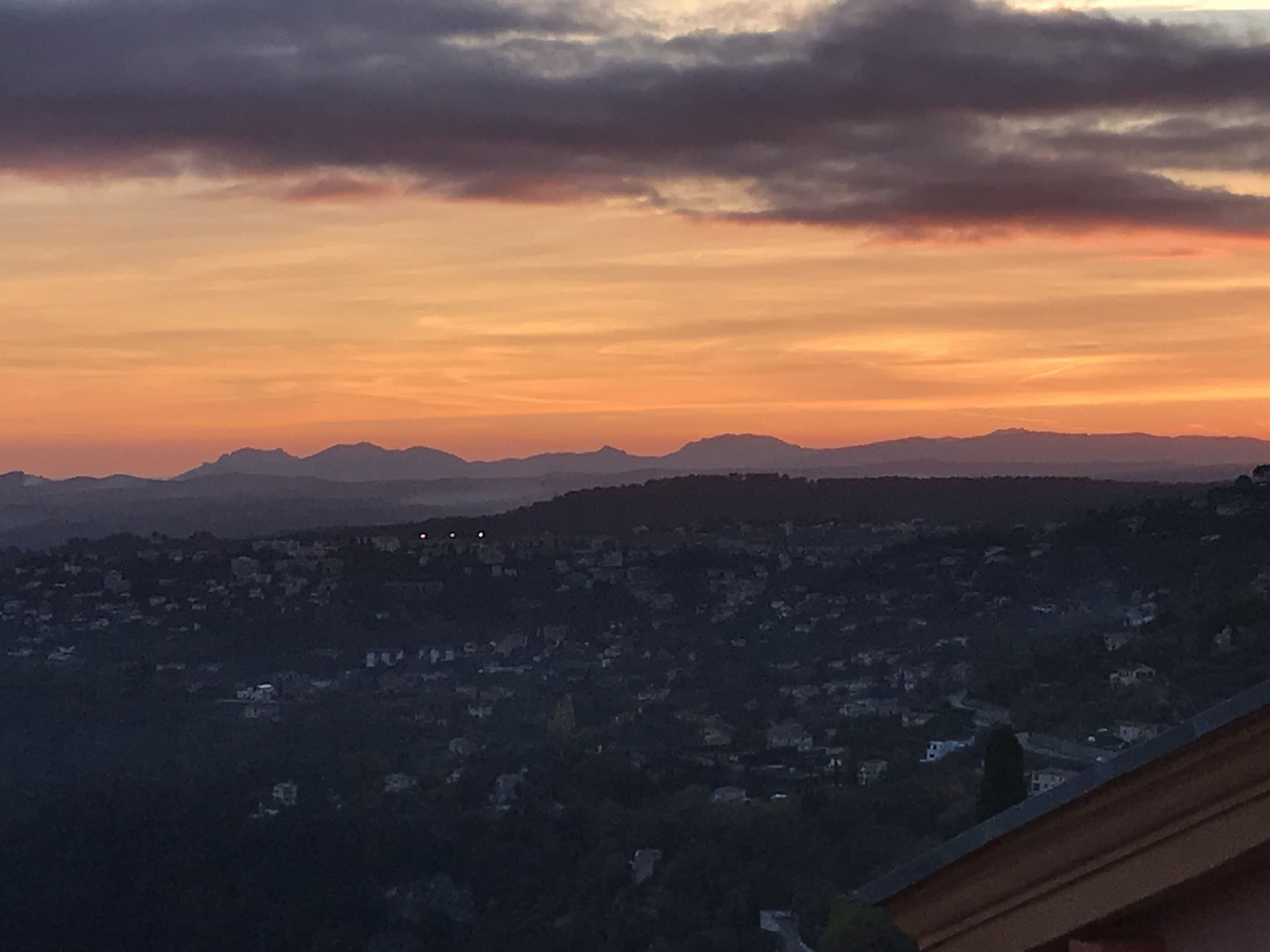 A panoramic view of a cityscape at sunset with mountains in the background.