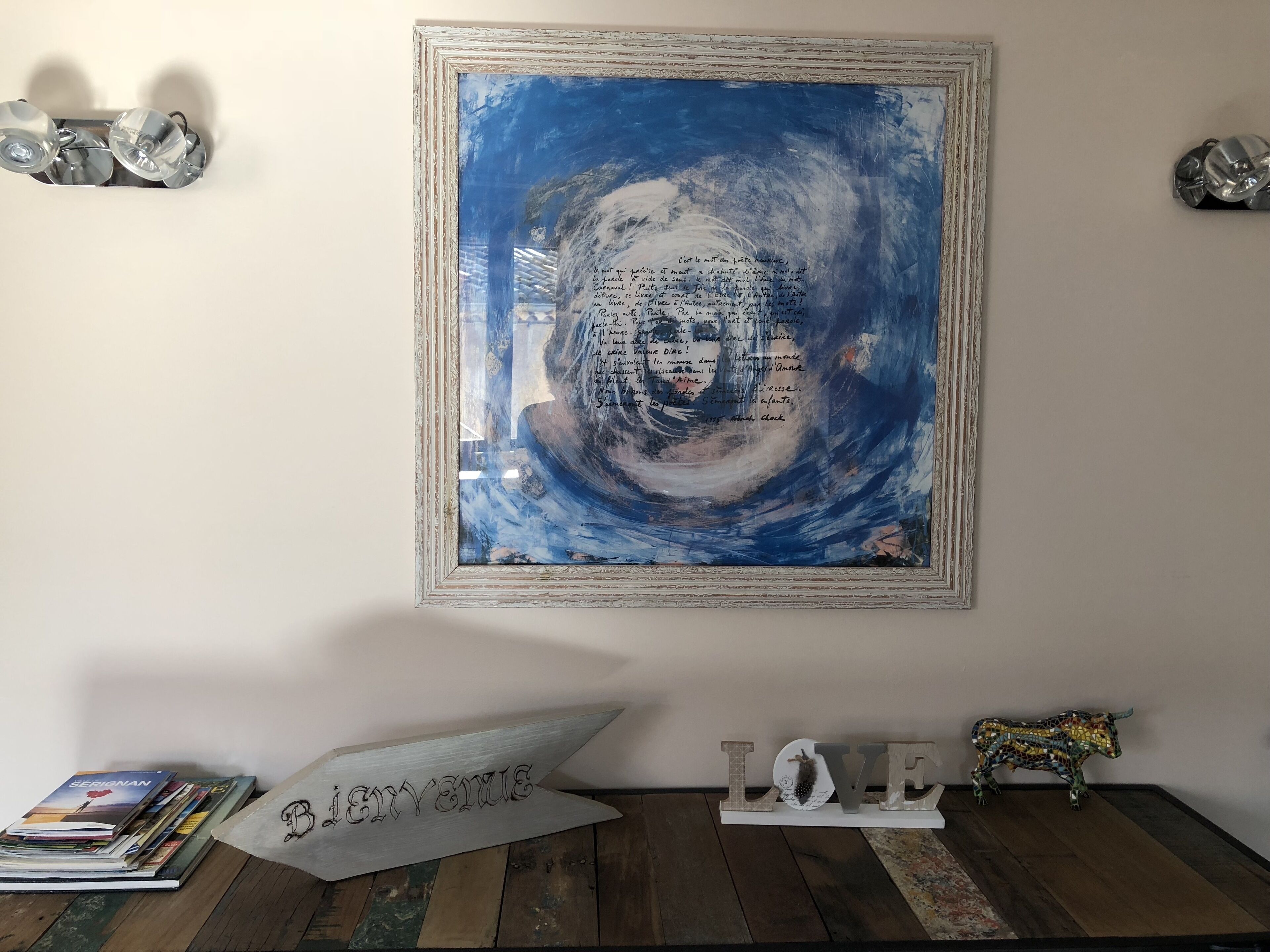 Une peinture abstraite encadrée avec du texte, un panneau décoratif en forme de flèche et un panneau « LOVE » orné d’une décoration en forme de taureau, le tout posé sur un plancher en bois.