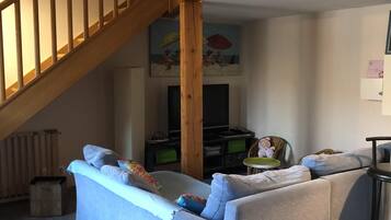 Un salon avec un escalier en bois, un canapé, une télévision et un tableau accroché au mur.