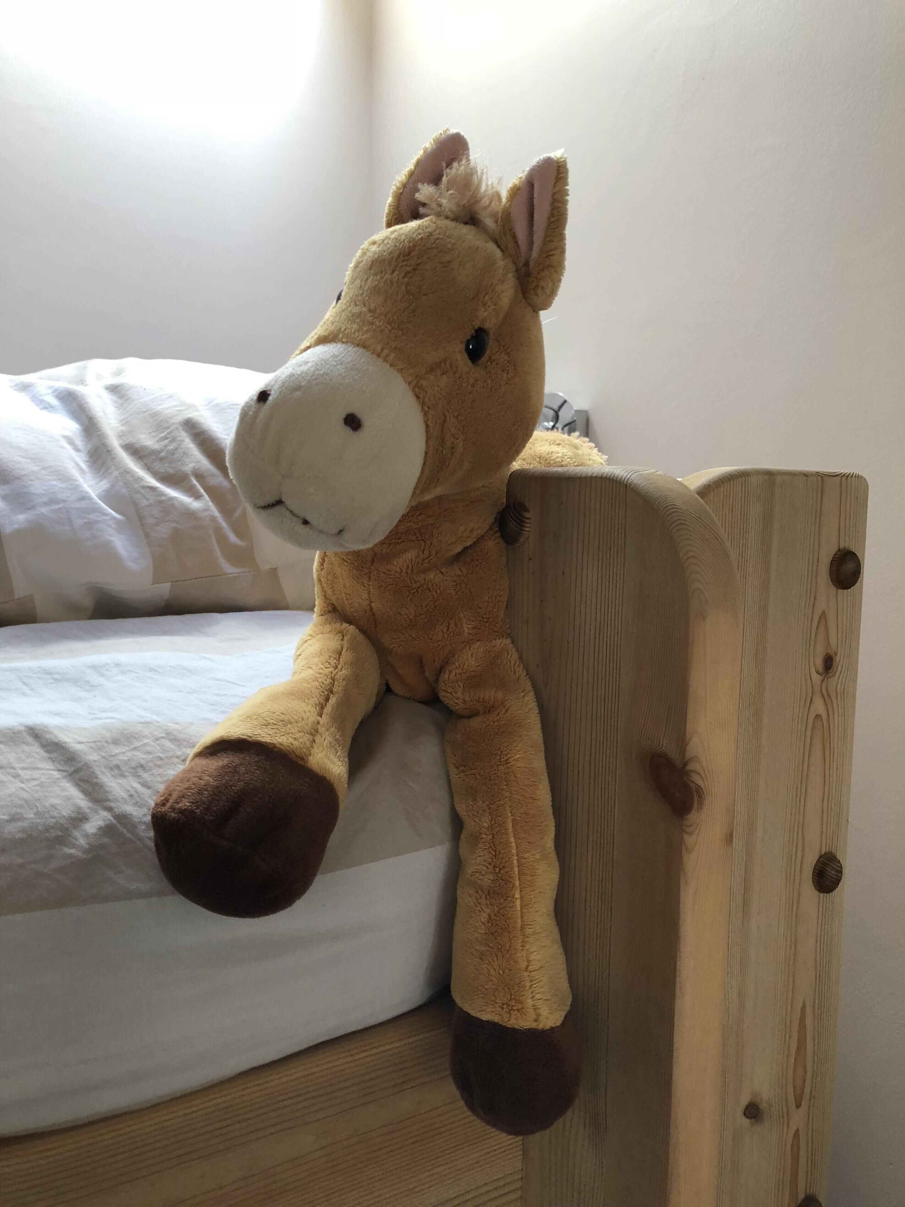 A plush toy giraffe on a wooden headboard of a bed.