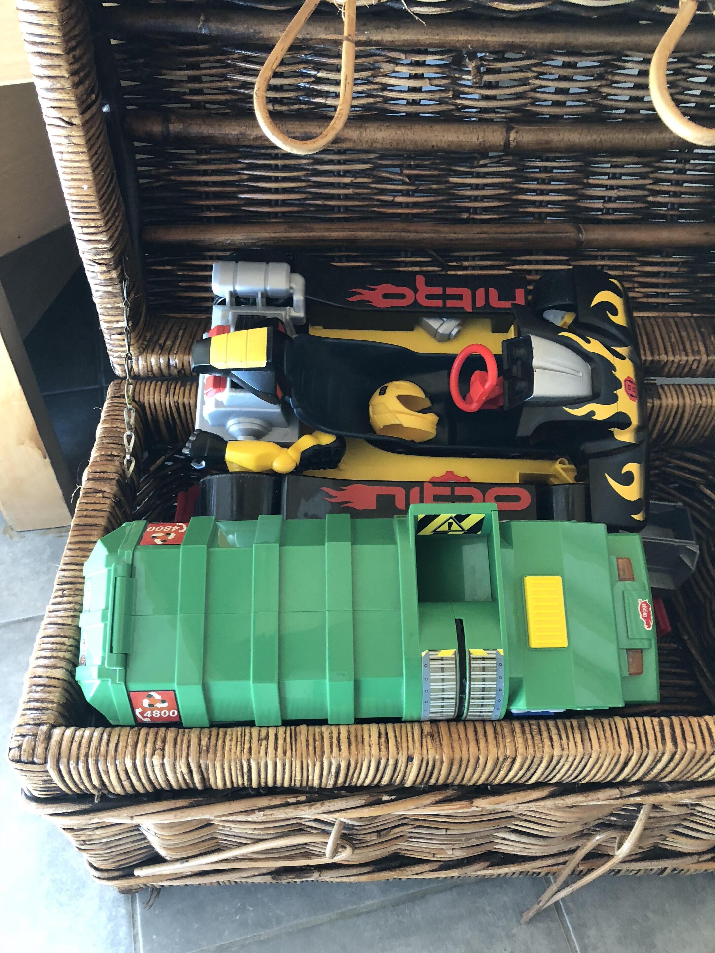 A wicker basket containing various toy vehicles and a green toy car.