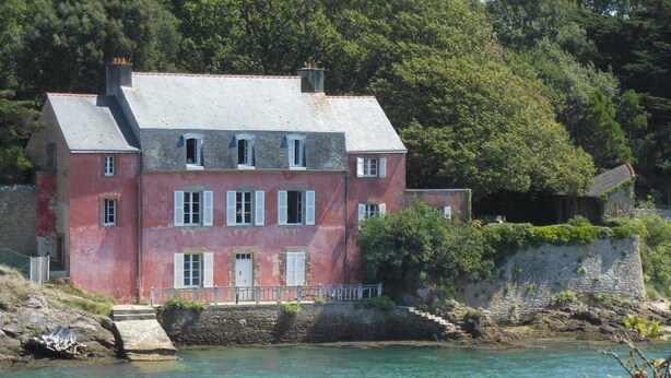 A red building with multiple windows and a stone wall beside a body of water. - Séné seaside lodging (classified 2 stars) (Séné)