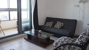 Een moderne woonkamer met een glazen salontafel, een grijze bank met decoratieve kussens, en een fauteuil met dessin.